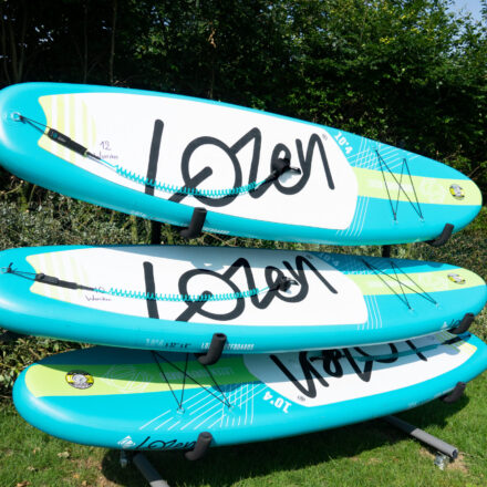 Drei Bretter sind auf einem Ständer geordnet. Es sind Stand-up-Paddling-Bretter. Die Bretter sind numeriert (12,10,13)