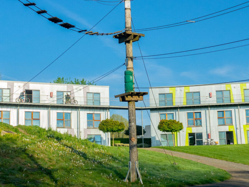 Bâtiment au milieu de la verdure et de la nature avec plusieurs chambres et, au premier plan, le parcours d'accrobranche.