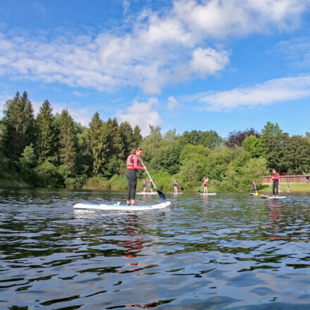 Mehrere Personen sind beim Stand-up-Paddling auf dem Bütgenbacher See – direkt am Bootshaus von Worriken.