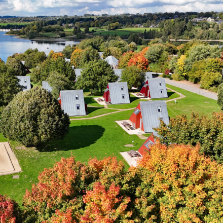 Ferienwohnungen vom Sport- und Ferienpark Worriken im Herbst. Auf dem Hintergrund ist den Staumauer vom Bütgenbacher See zu sehen.