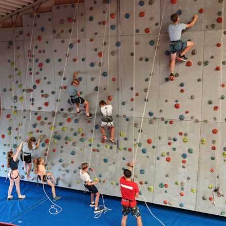 Kinder sind am klettern auf einer Indoor Klettermauer.