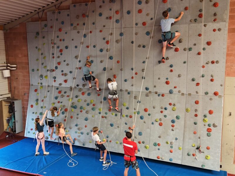 Kinder sind am klettern auf einer Indoor Klettermauer.