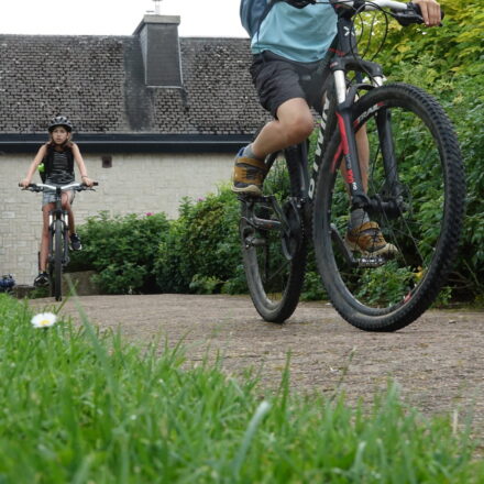 Kinder auf dem Fahrrad auf einem Weg mit auf dem Hintergrund ein Gebäude mit einem Schild Restaurant Mercator