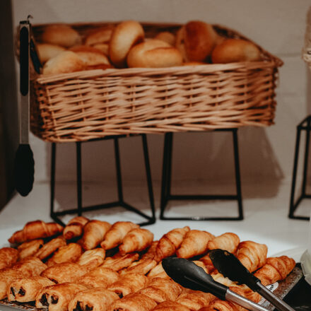 Schale mit Schokoladenbrötchen und einem Greifer. Im Hintergrund: ein Korb mit Pistolets. Sieht aus wie ein Teil eines Frühstücksbuffets.