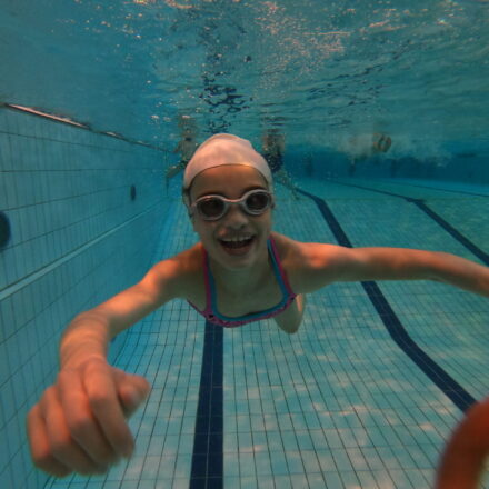 Mädchen unter Wasser in einem Schwimmbad mit Schwimmbrille. Sie lacht und hat es gut.