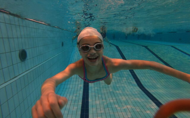 Mädchen unter Wasser in einem Schwimmbad mit Schwimmbrille. Sie lacht und hat es gut.