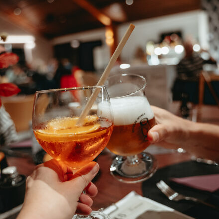 Zwei Gläser, die höchstwahrscheinlich Bier und ein anderes alkoholisches Getränk enthalten, in den Händen von zwei Personen, die anscheinend einen Toast ausbringen