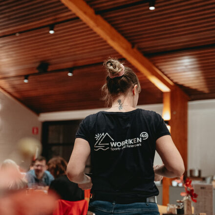 Frau bedient in einem Restaurant. Ihr Rücken ist sichtbar. Die Frau trägt ein T-Shirt mit der Aufschrift „Worriken“.