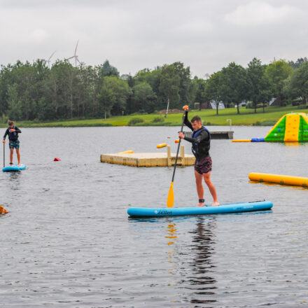 Mehrere Personen sind beim Stand-up-Paddling auf dem Bütgenbacher See – direkt am Strand von Worriken, dem VENNtastic Beach.