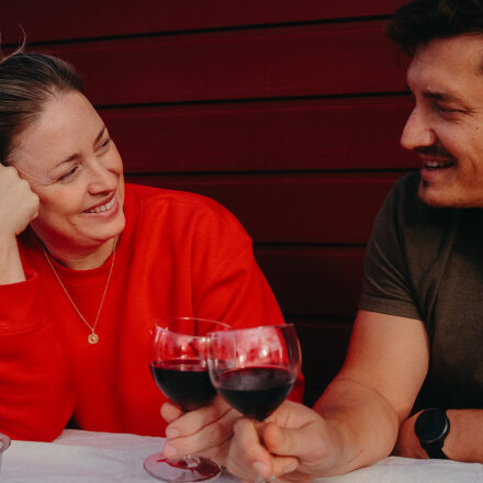 Ein Mann und eine Frau vor einer Fassade mit roten Bekleidung so wie es typisch ist für den Ferienwohnungen in Worriken. Die 2 Personen haben es gut weil sie lachen und heben ein Weinglas